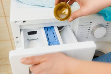Sıvı toz deterjanı ve ölçü kabının makineye dökülmesi. Ev işleri, çamaşır yıkama, obezite konsepti..