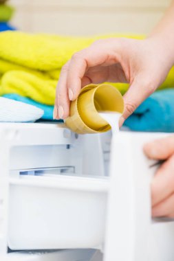 Çamaşır yıkarken, kapaktan çamaşır makinesine kumaş yumuşatıcısı dökerken..