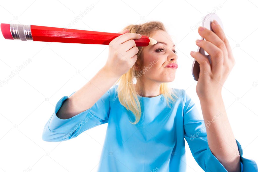 Funny silly woman trying to paint her eyebrows using big huge oversized regular student pencil. Make up fun concept.