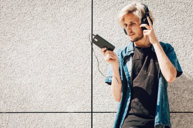 Erkek moda, teknoloji, kentsel tarzı giyim kavramı. Şehir sokak giyen kot kıyafeti ve müzik ve telefon tutarak güneş gözlüğü üzerinde duran hipster adam