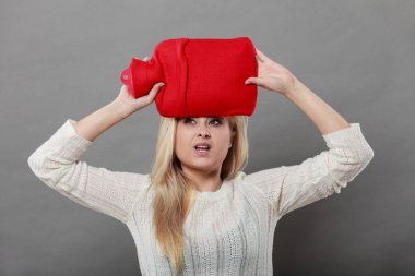 Baş ağrısı ile başa çıkmak için kırmızı sıcak su şişesi üzerinde kafa tutan kadın