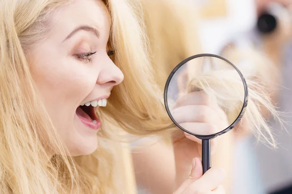 Happy woman magnifying her hair ends looking through magnifer being positive about conditioner results on her hairdor.