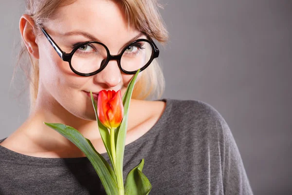 Beauty emotions nature passion glasses concept. Nerdy girl snffing flower. Young blonde casual lady holding smelling red tulip.