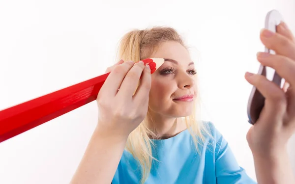 Funny silly woman trying to paint her eyebrows using big huge oversized regular student pencil. Make up fun concept.