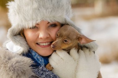 Genç bir kadın dışarıda karda eğleniyor. Dişi, soğuk kış gününde safkan köpek yavrusuyla oynuyor..