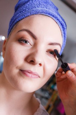 Görünüm konsepti. Islak saçlara havlu takıp göz kapaklarına makyaj yapan bir kadın. Profesyonel sanatçının fırçasıyla rimel sürülüyor