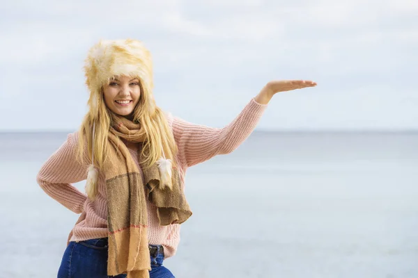 コピースペースを指している秋の天気の間にビーチで10代の女性が屋外で過ごす時間 セーター スカーフ 毛皮の帽子を身に着けて — ストック写真
