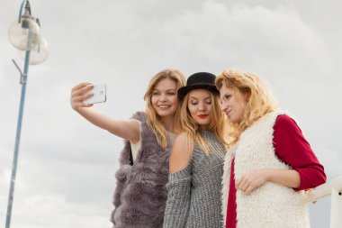 Üç kadın selfie çekiyor, dışarıda eğleniyor, fotoğraf çekmek için akıllı telefon kullanıyor..