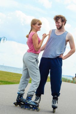 Aktif tatiller, egzersizleri, ilişki kavramı. Kadın ve adam ayakta ve birbirlerine, ona işaret eden kız arıyorum rollerskates giyiyor