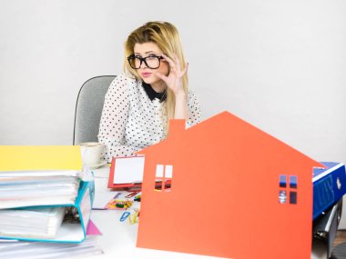 Masada oturan iş kadınının dosyalarla dolu evraklarla dolu olduğunu, büyük kırmızı bir evi olduğunu, emlak konsepti olduğunu düşünüyor..