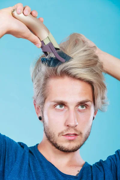 Hairdo hairstyle concept. Cool male hairstylist making self trendy haircut, fashion blonde metrosexual model going to shave his long hair