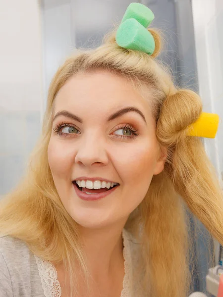 Blonde woman using hair rollers to create beautiful hairstyle on her hairdo.