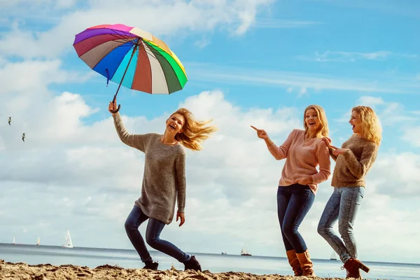 Three women full of joy having great time together. One woman holding colorful umbrella.