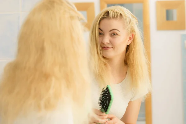 Женщина расчесывает свои светлые волосы в ванной — стоковое фото