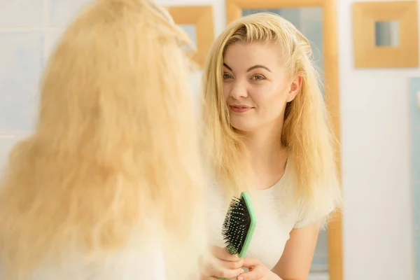 Woman brushing her blonde hair in bathroom