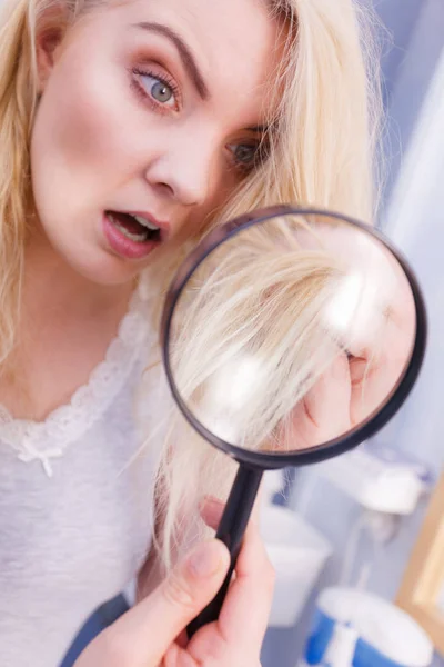 Woman looking at hair ends through magnifying glass