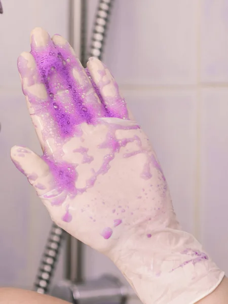 Persoon die paarse shampoo op witte latex handschoenen — Stockfoto