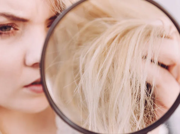 Woman looking at hair ends through magnifying glass