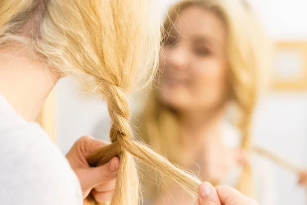 Женщина делает косички на светлых волосах — стоковое фото