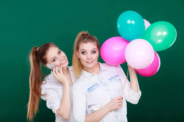 Two girls with mobile phone and balloons — Stock Photo, Image