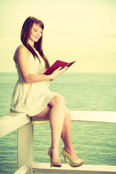 Mulher sentada no obstáculo perto do mar, livro de leitura — Fotografia de Stock