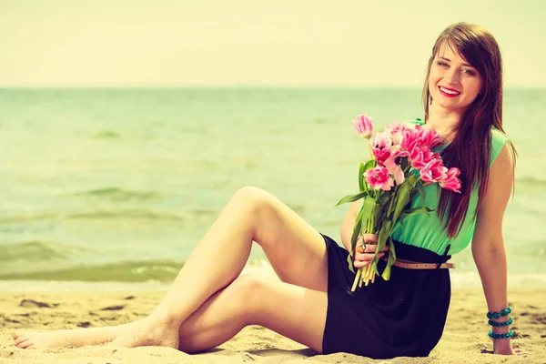 Mujer sosteniendo ramo de flores sentado en la playa —  Fotos de Stock