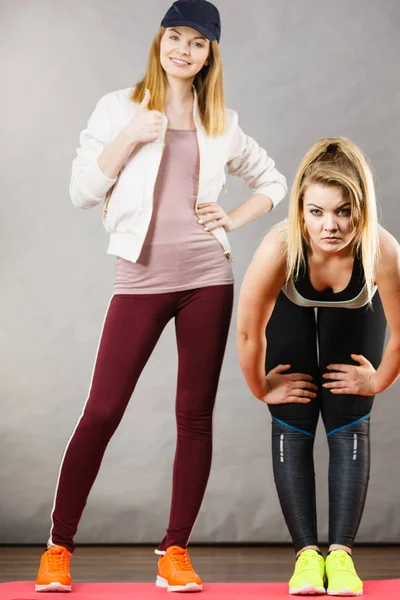 Vrouw in sportkleding uitrekken poten met trainer — Stockfoto