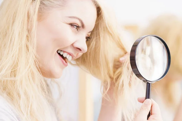 Happy woman looking through magnifer at hair