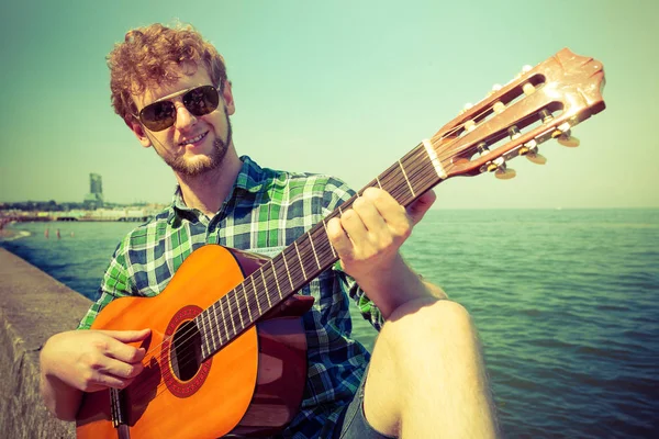 Joven hipster tocando la guitarra por mar océano . — Foto de Stock