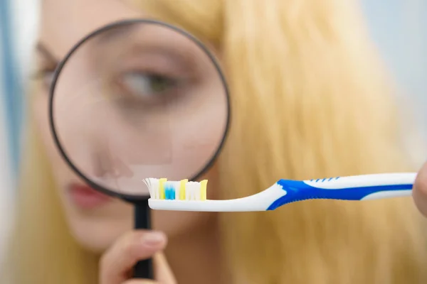 Mulher olhando escova de dentes através da lupa — Fotografia de Stock