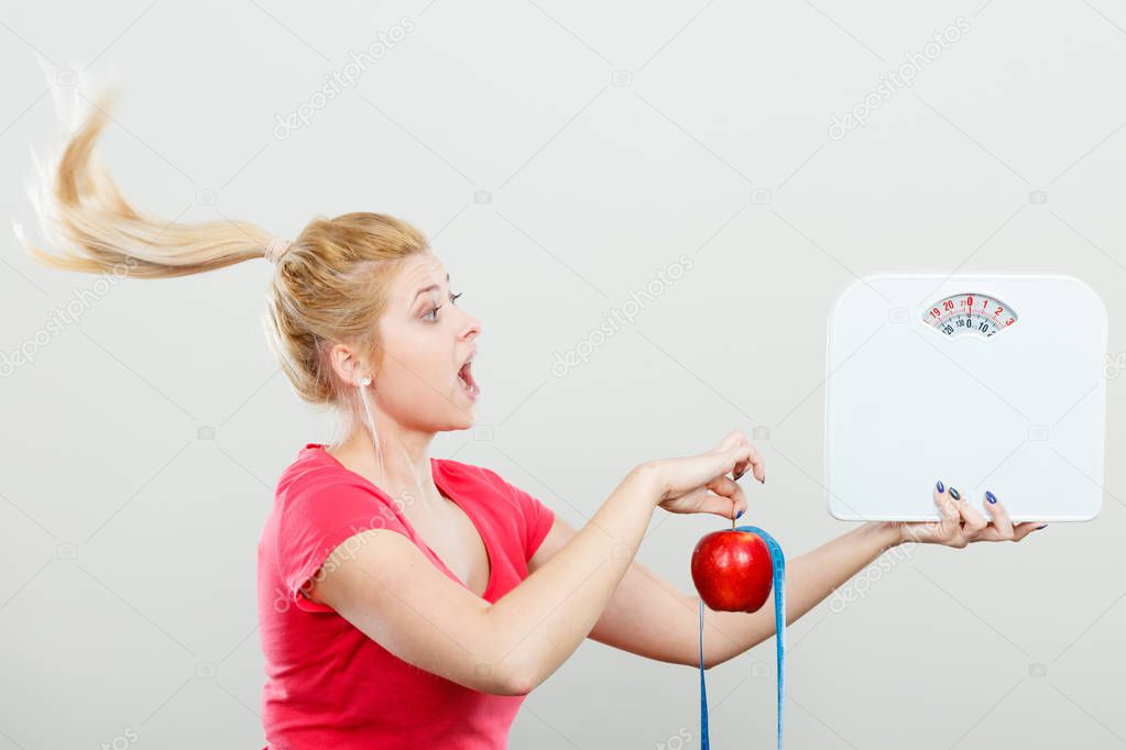 Woman holding apple,measuring tape and weight machine