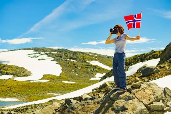 Turist dağlarda kamera ve Norveç bayrağı tutar — Stok fotoğraf