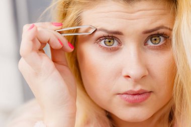 Kaşlarını cımbızla temizleyen kadın.