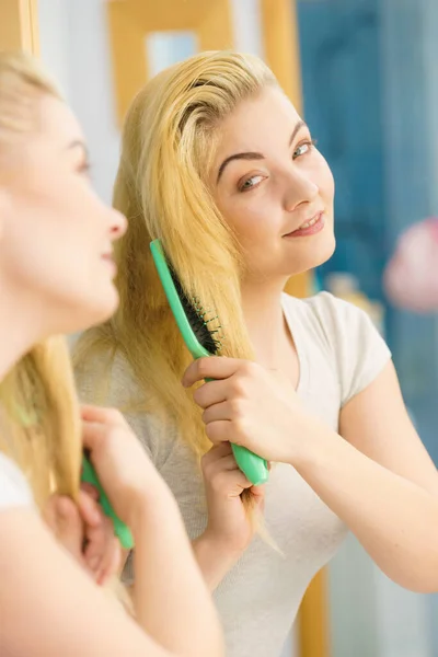 Femme brossant ses cheveux blonds dans la salle de bain — Photo