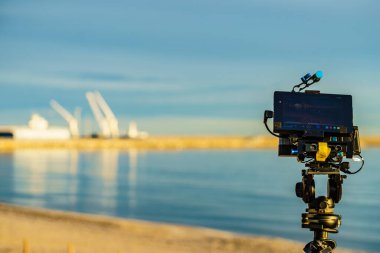 Tripod üzerindeki kamera sanayi manzarası ve deniz limanından fotoğraf çekiyor. Gandia, Valencia İspanya yakınlarındaki plajdan görüntü