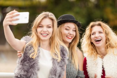 Üç kadın selfie çekiyor, dışarıda eğleniyor, fotoğraf çekmek için akıllı telefon kullanıyor..