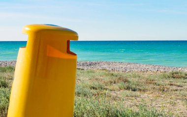 Deniz manzarası. Sarı çöp kutusu ya da çöp tenekesi olan İspanyol sahili. Kumsalı temiz tutmak..