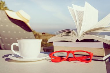 Tatillerde kitap okumak. Kahve fincanı ve kitaplar açık havada mavi deniz suyuna karşı. Kitap sayfaları rüzgarda çırpınıyor.