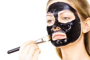 Siyah detoks detoks ile uygulanan genç bir kadın maskesini yüzüne doğru sıyırdı. Deriyle ilgilenen bir kız. Güzellik tedavisi. Cilt bakımı.