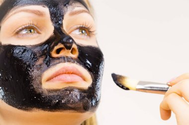 Yüzüne siyah detoks çamur maskesi süren genç bir kadın. Deriyle ilgilenen bir kız. Güzellik tedavisi. Cilt bakımı.