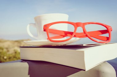 Tatillerde kitap okumak. Kahve fincanı ve kitap açık havada mavi deniz suyuna karşı sandalyede..