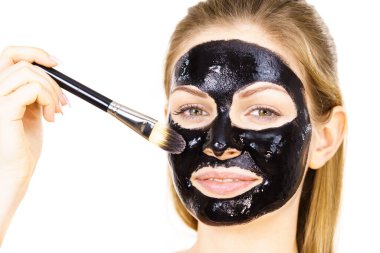 Siyah detoks detoks ile uygulanan genç bir kadın maskesini yüzüne doğru sıyırdı. Deriyle ilgilenen bir kız. Güzellik tedavisi. Cilt bakımı.