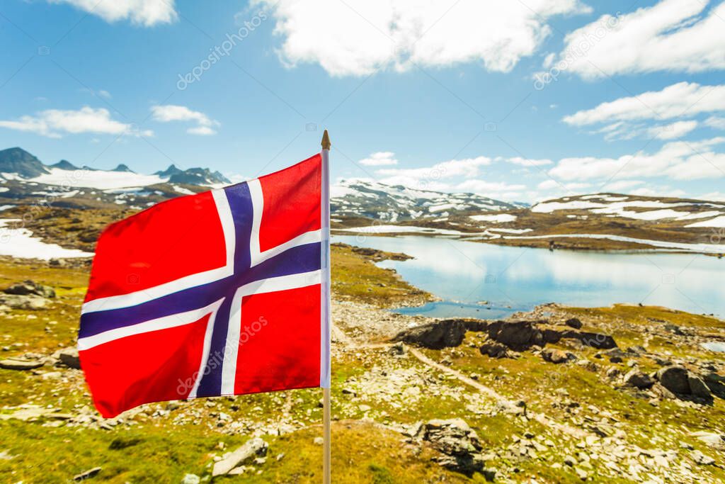 Norwegian flag waving against snowy mountains landscape, summertime. National tourist route Sognefjellet.