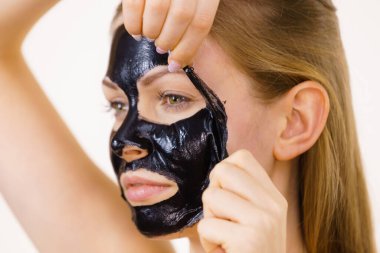 Karbonhidratlı siyah maskesini yüzünden, beyazın üstüne çıkaran genç bir kadın. Genç kız yağlı cildiyle ilgileniyor, gözenekleri temizliyor. Güzellik tedavisi. Cilt bakımı.