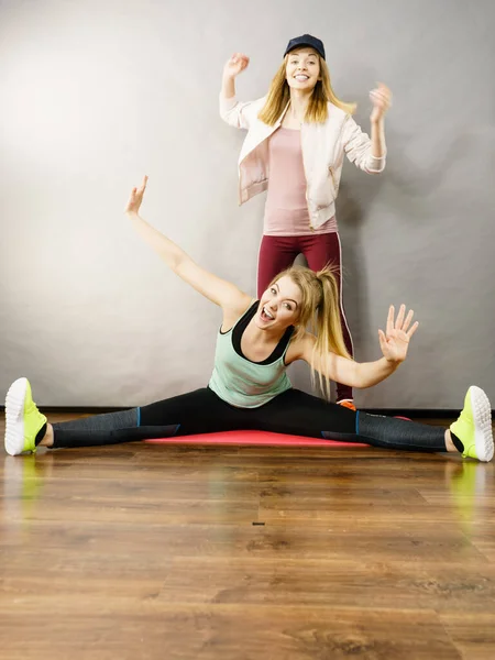 スポーツウェアのストレッチボディの若いブロンドの女性は 彼女の女性トレーナーと一緒に働いています 家でのトレーニング フィット感と健康 — ストック写真