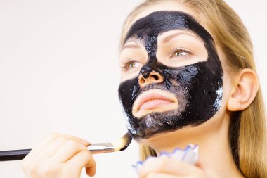 Yüzüne siyah detoks çamur maskesi süren genç bir kadın. Deriyle ilgilenen bir kız. Güzellik tedavisi. Cilt bakımı.