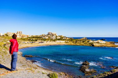 İspanyol deniz kıyısında dinlenen turist kadın. Akdeniz kıyısı manzarası, Murcia bölgesindeki kıyı şeridi. Cabo de Palos 'ta Cala Reona.