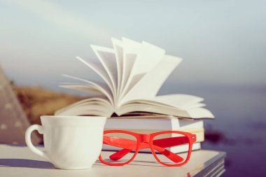 Tatillerde kitap okumak. Kahve fincanı ve kitaplar açık havada mavi deniz suyuna karşı. Kitap sayfaları rüzgarda çırpınıyor.