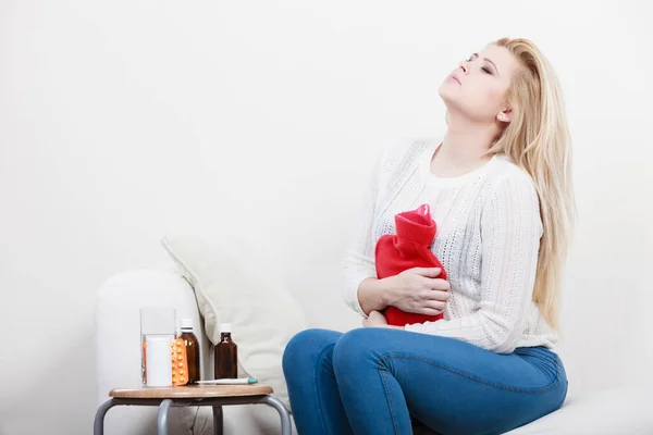 疼痛时期和月经抽筋问题的概念 有肚子痛的女人坐在沙发上感觉很不舒服 拿着热水瓶来解闷 — 图库照片
