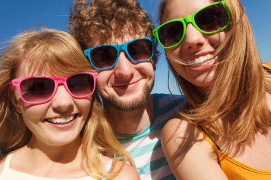 Arkadaşlık mutluluğu yaz tatili konsepti. Bir grup arkadaş, renkli güneş gözlüklü iki kız, dışarıda eğleniyorlar, neşeli bir havaları var..